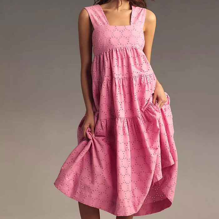 A pink dress with a geometric pattern is held by a person against a neutral grey background.