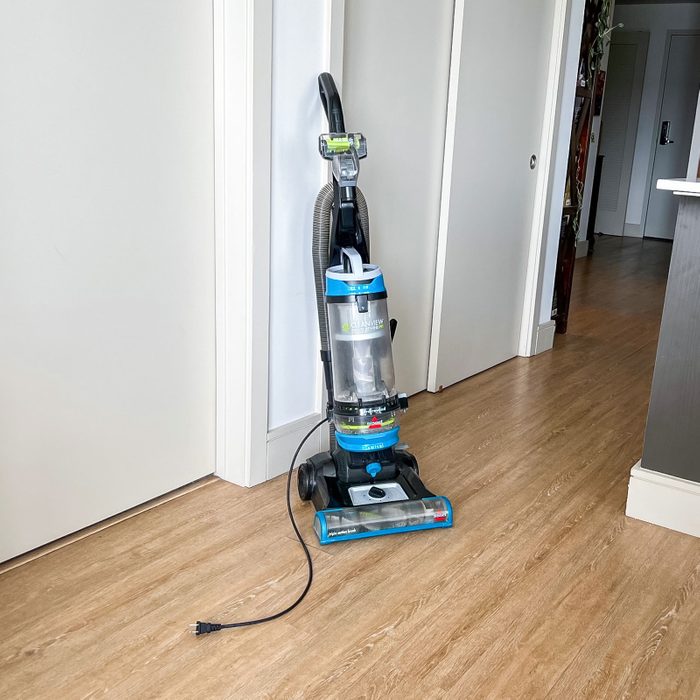 Vacuum cleaner stands upright, unplugged, in a hallway with wooden flooring and white walls. Text: â€œCleanViewâ€ on the vacuum.