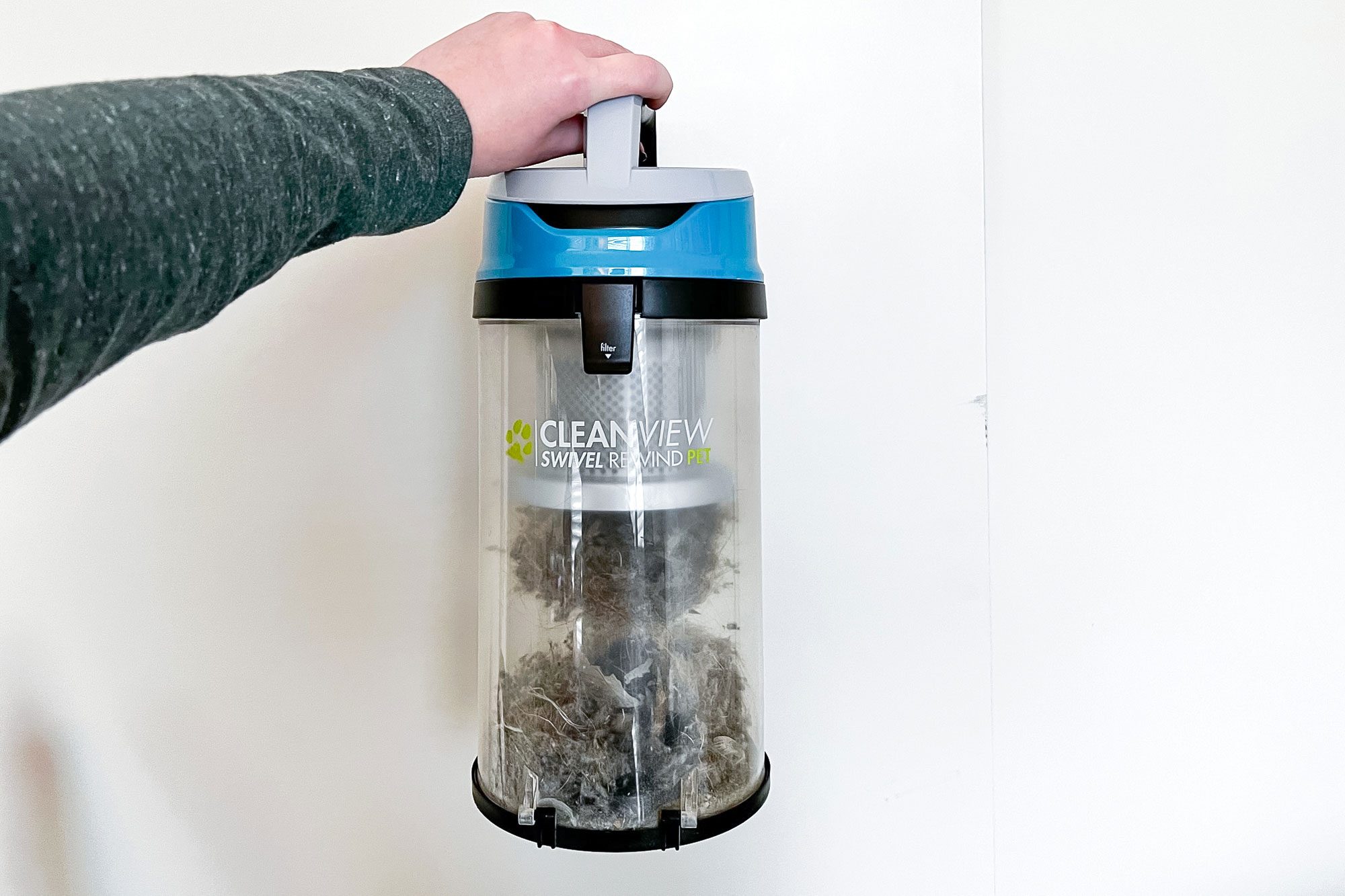 Hand holds a vacuum dust canister containing debris; labeled "CLEANVIEW SWIVEL REWIND PET," against a plain white background.