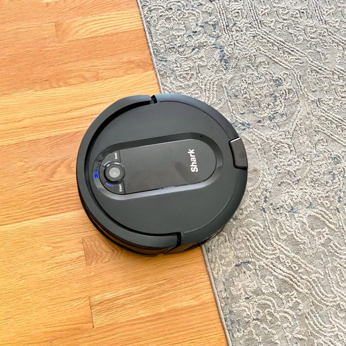 Robot vacuum cleaning, moving across hardwood and patterned rug, labeled 
