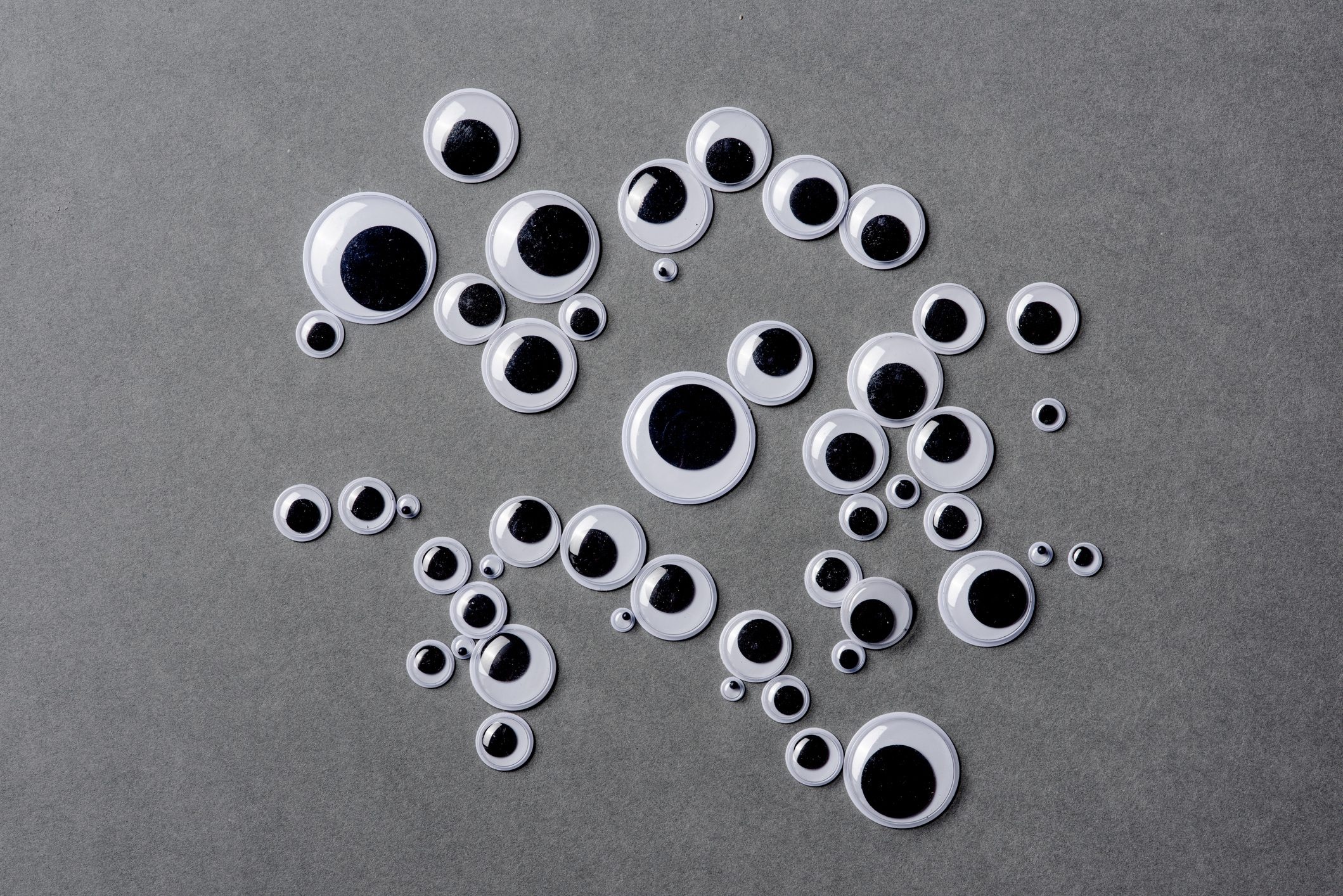Many different sizes of googly eyes on grey background.