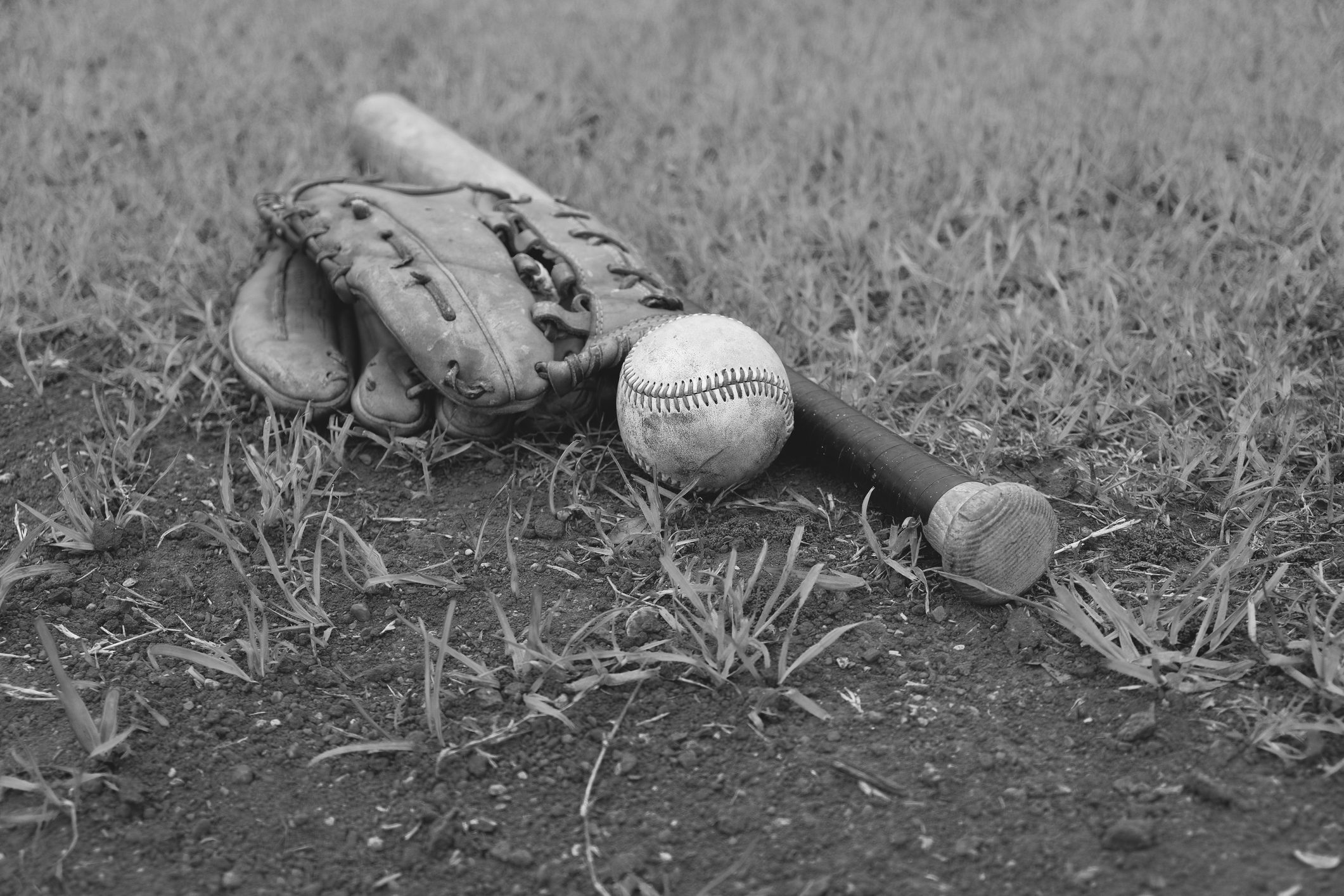 Baseball gear lies on grass; a glove, bat, and ball rest together on the ground, creating a vintage sports scene.