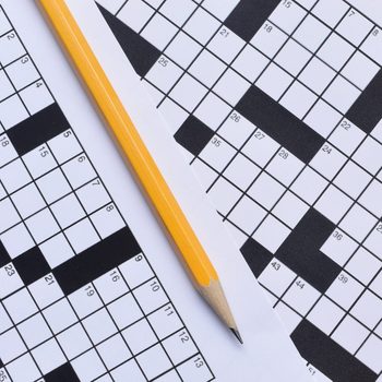 Pencil resting on two overlapping crossword puzzles, featuring numbered black and white squares.