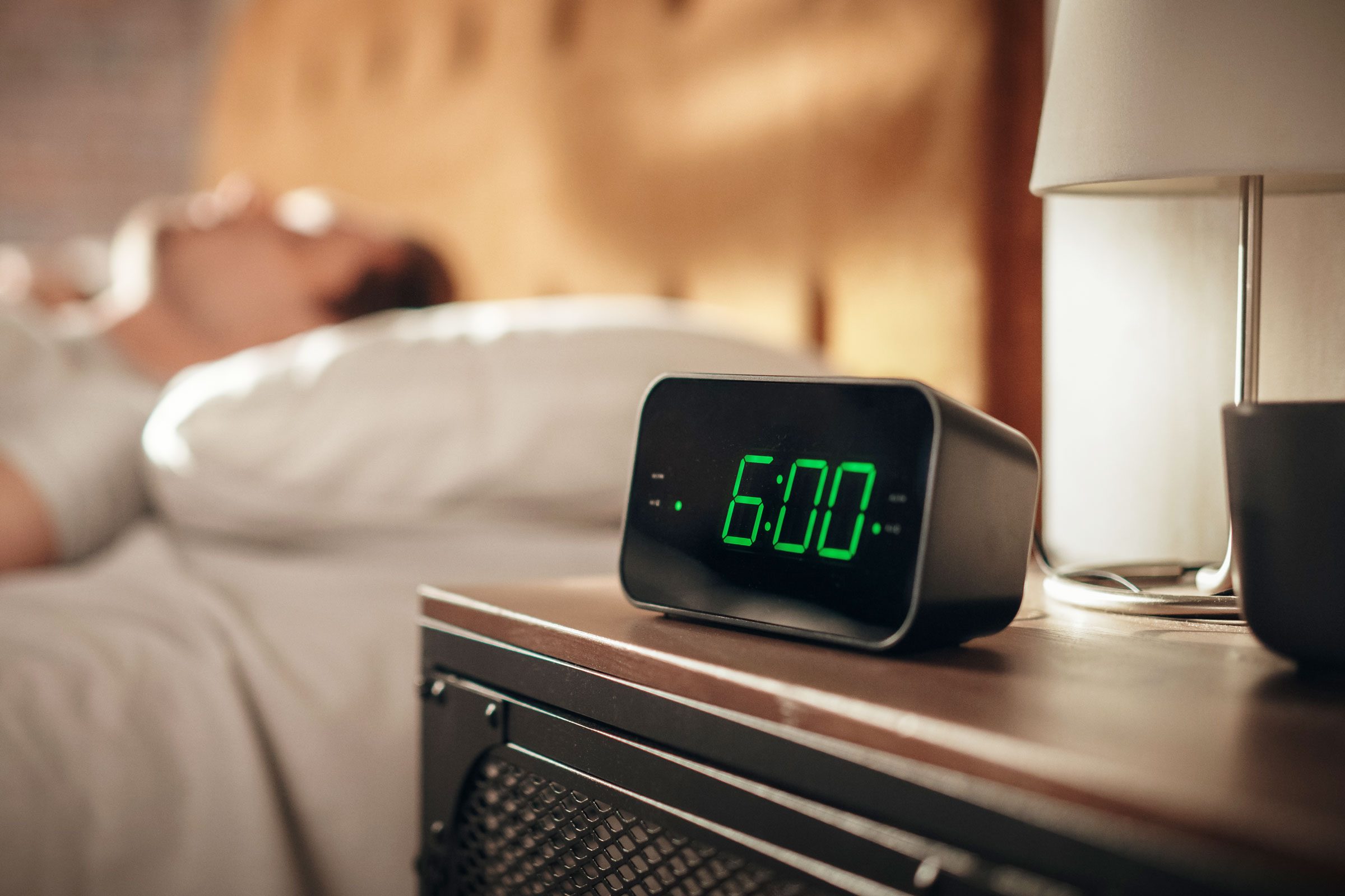 alarm clock that says 6am with sleeping man in background