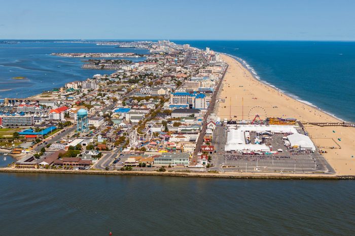 Coastal cityscape features buildings and amusement park lining the sandy beach, adjacent to the ocean, under a clear blue sky.