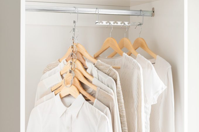 Cohesive Wardrobe Collection in Neutral Palette, Featuring a Variety of Textured Tops and Sweaters on Wooden Hangers, Neatly Organized in a Clean White Closet, Serene Clothing Storage Atmosphere.