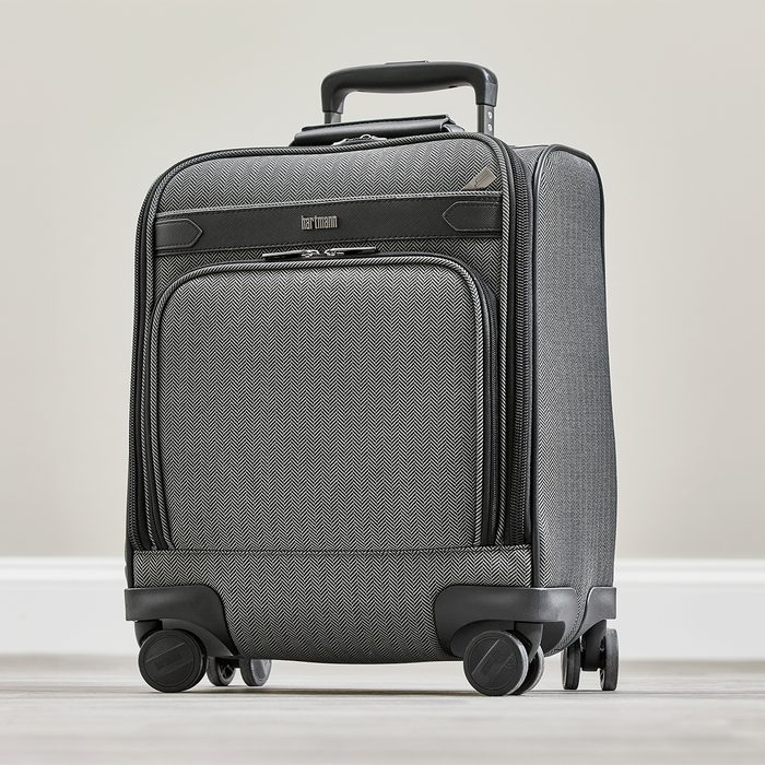 Suitcase stands upright on four wheels; gray zigzag pattern, black handle extended in neutral indoor setting.