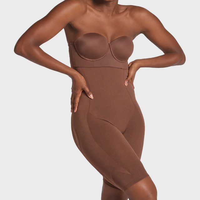Woman wearing brown strapless shapewear adjusts her posture against a plain white background.