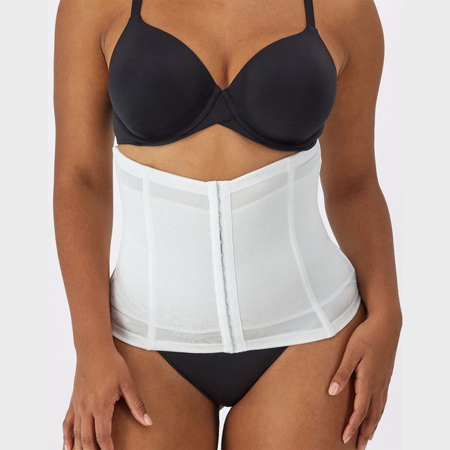White corset hugs waist, providing structure; worn over black lingerie, against plain gray background.