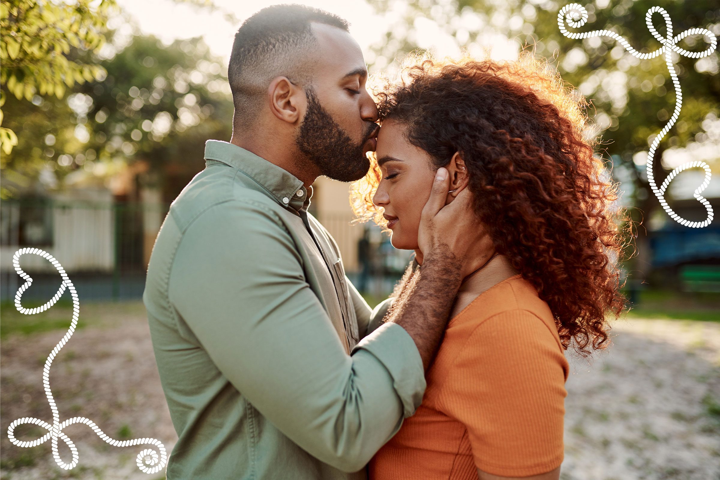 Man kisses woman's forehead, embracing gently in a sunlit park, surrounded by greenery and whimsical heart doodles.