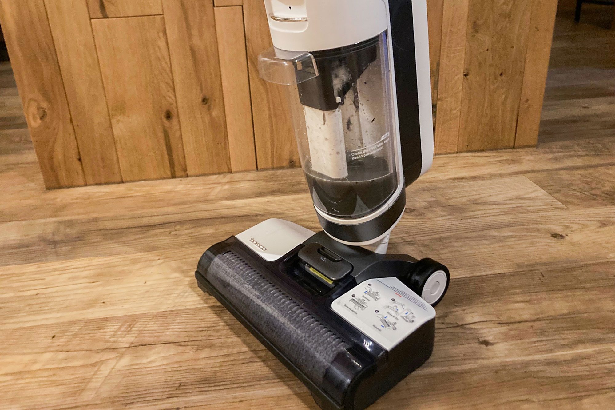 Vacuum cleaner sits idle on wooden floor, featuring a transparent dust container.