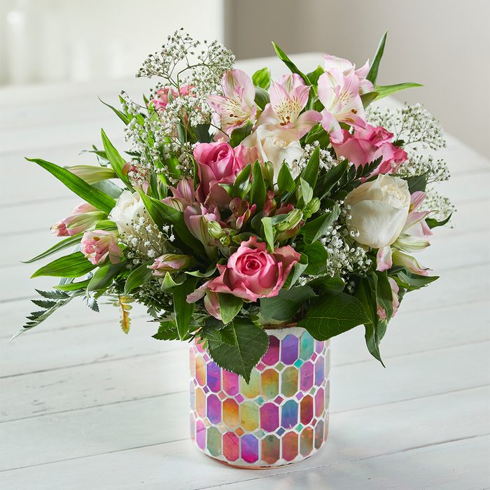 Bouquet of pink and white flowers arranged in a colorful hexagon-patterned vase on a white wooden table.