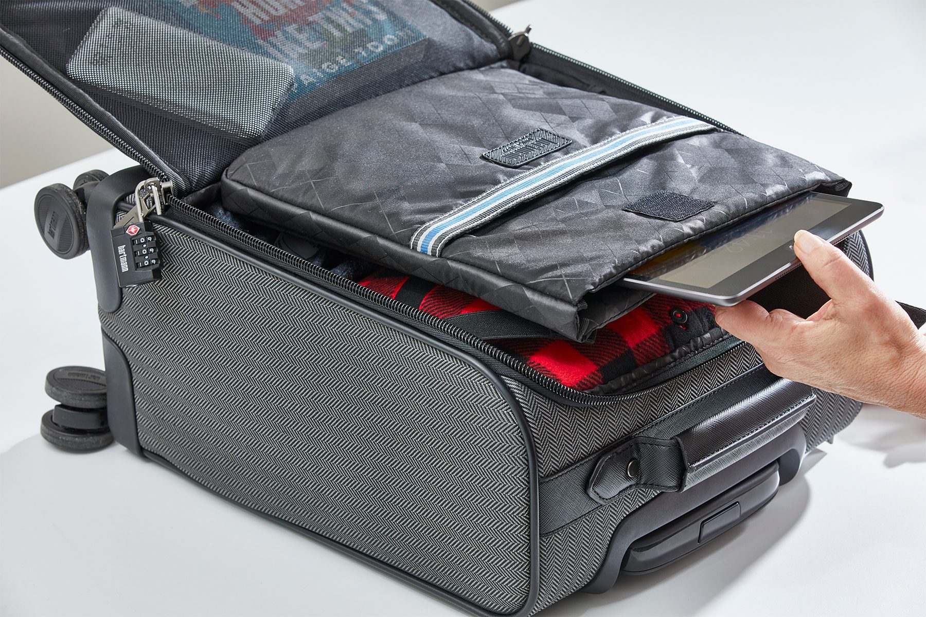 Suitcase reveals tablet being inserted, surrounded by clothing and zipper compartment. Secure setting includes a combination lock on the zipper.