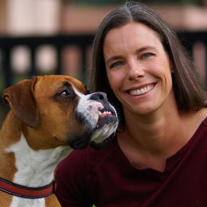 Dog gazes affectionately at smiling woman, both in a garden setting with blurred greenery in the background.