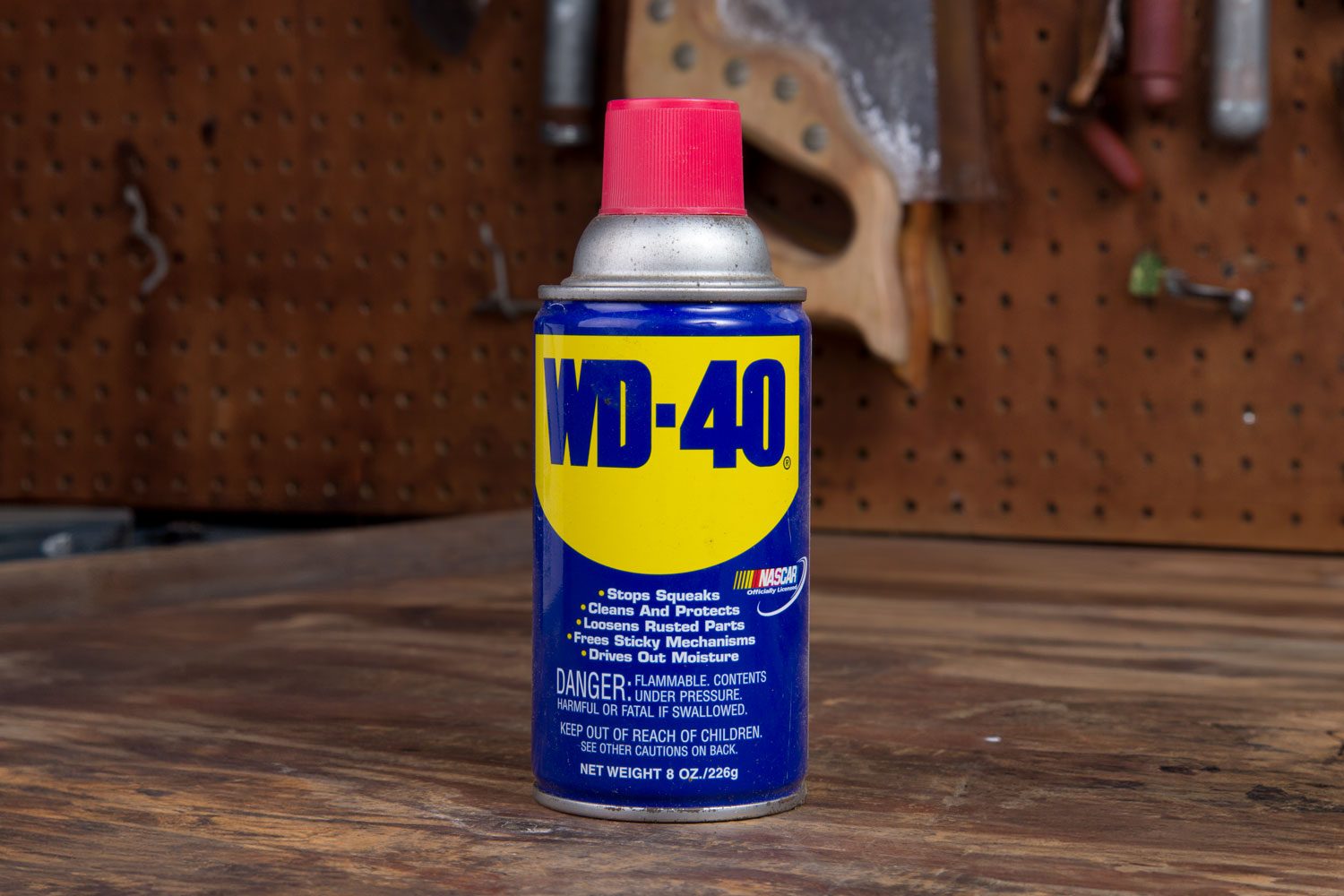 WD-40 can sits on a wooden workbench, surrounded by tools on a pegboard.