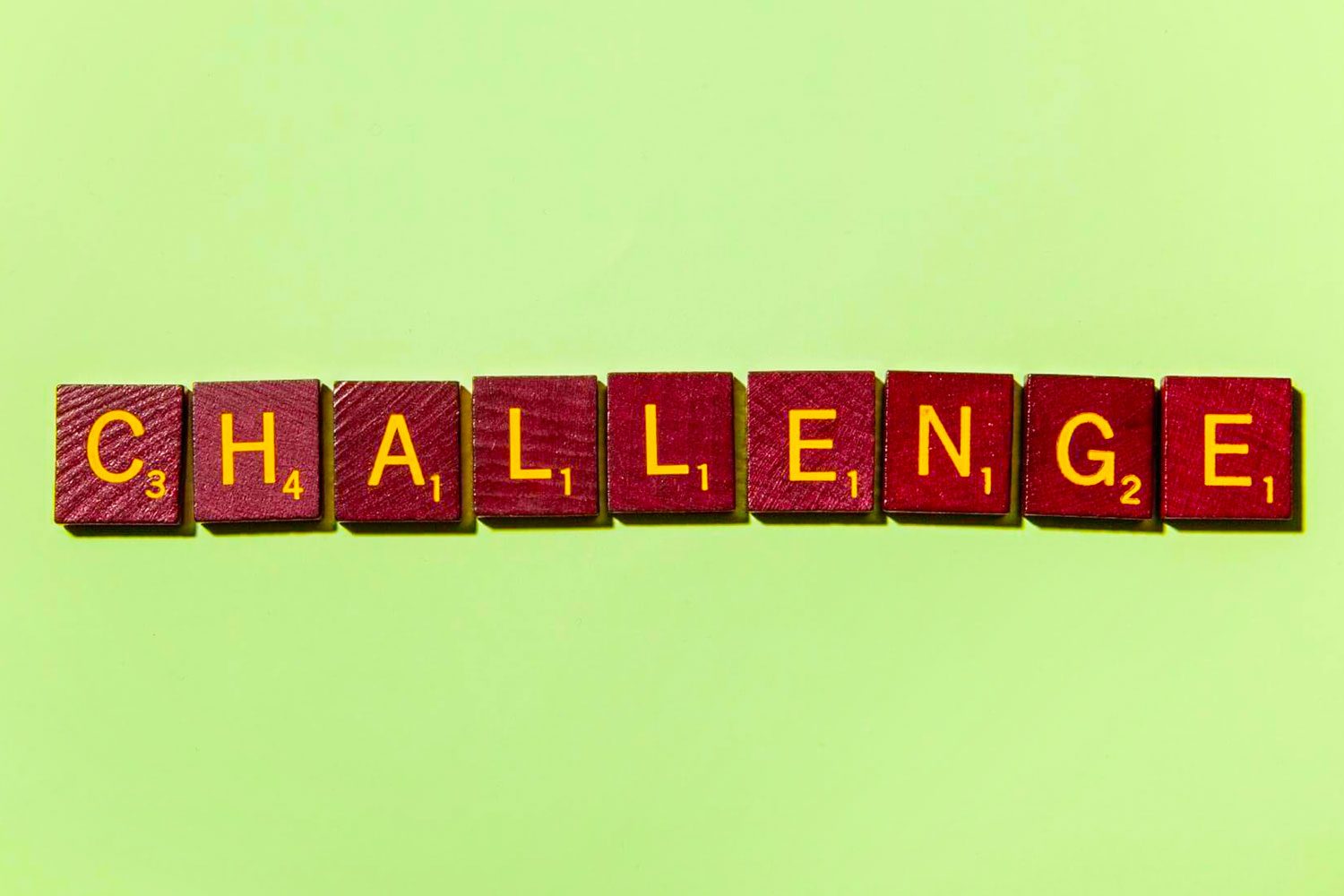 Scrabble tiles spell "CHALLENGE," arranged horizontally on a light green background.