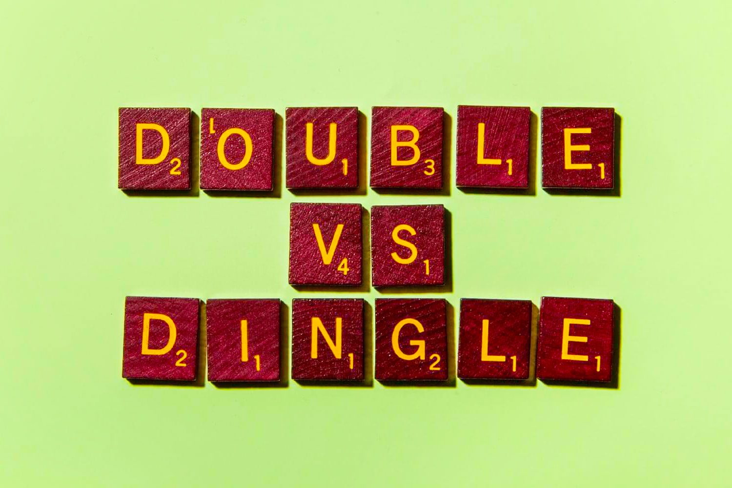 Wooden letter tiles spell "DOUBLE VS DINGLE" against a light green background.