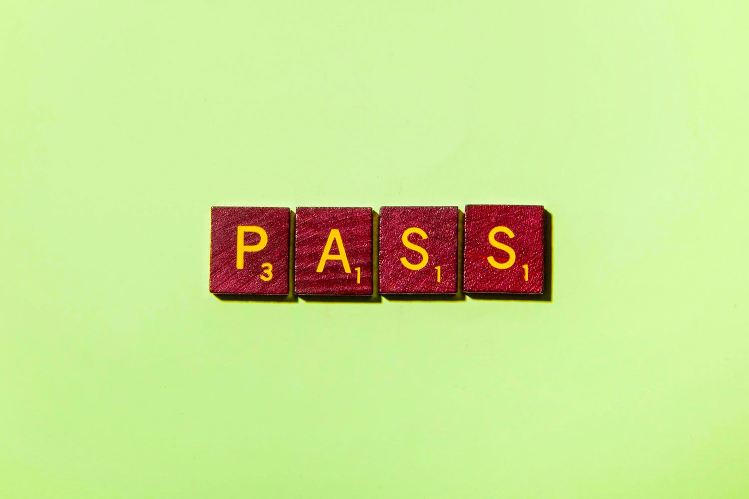 Red Scrabble tiles spell "PASS" on a light green background.
