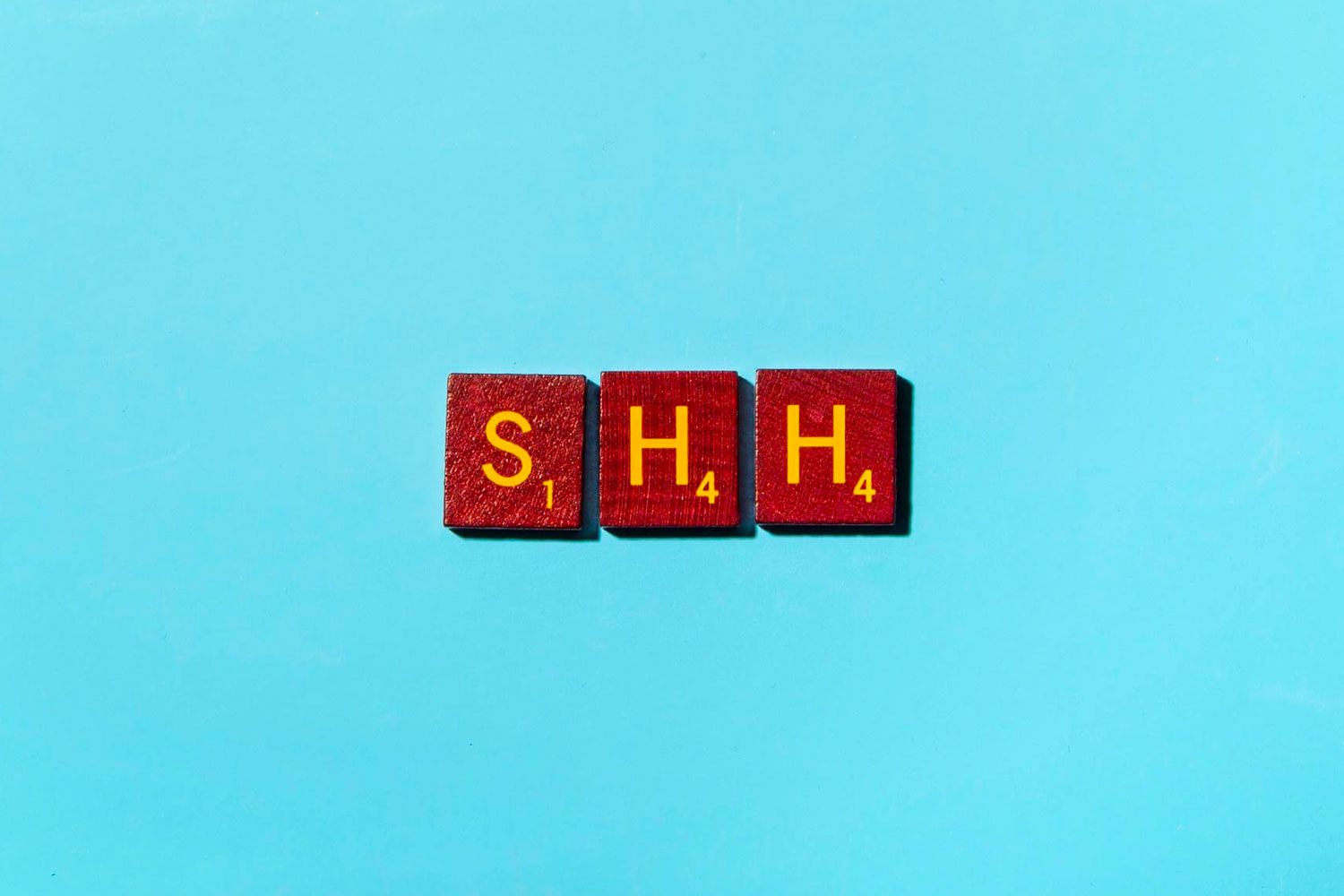 Red letter tiles spell "SHH," placed against a bright blue background.