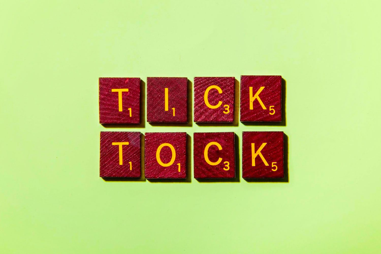 Red Scrabble tiles spell "TICK TOCK" on a light green background.