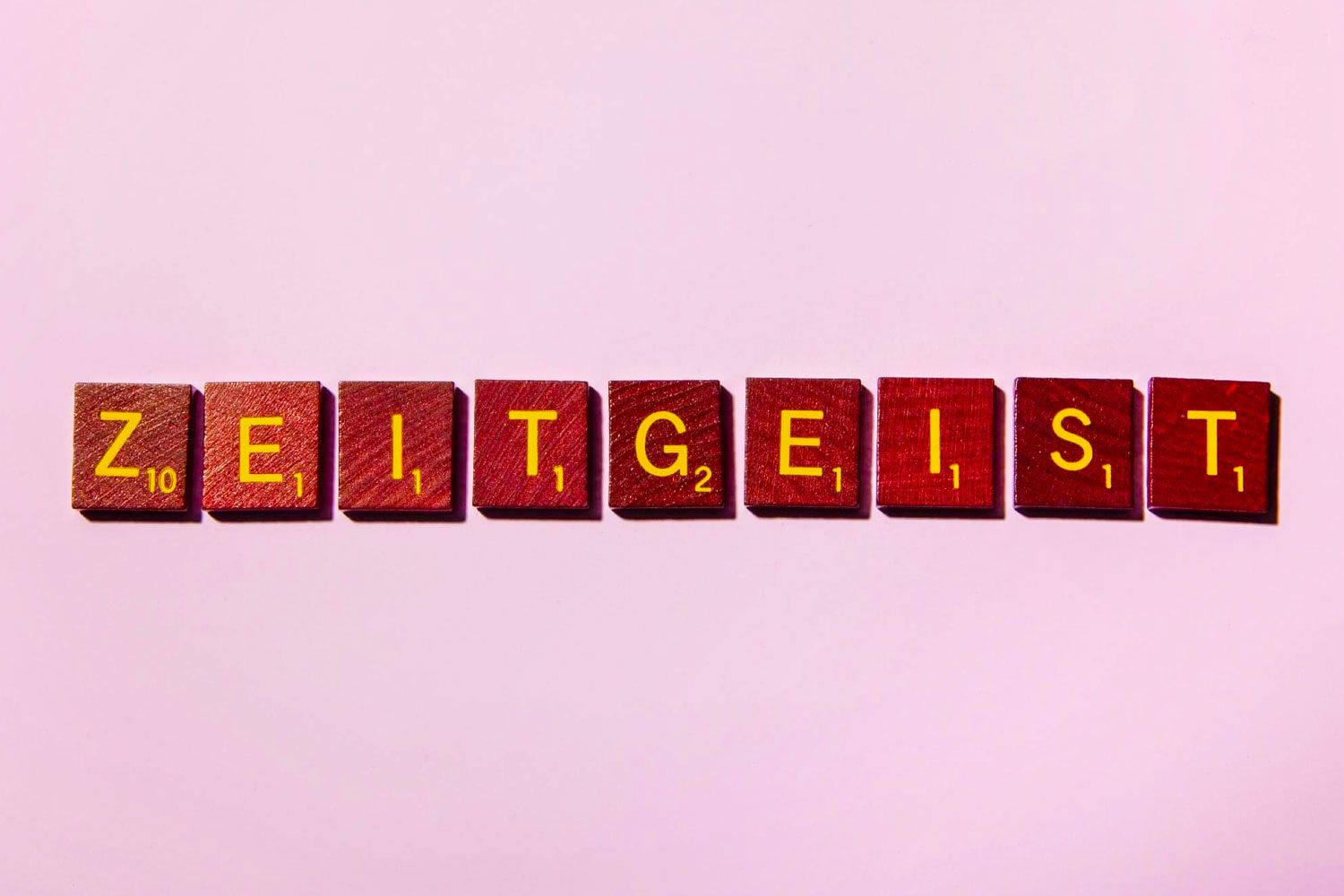 Wooden letter tiles spell "ZEITGEIST" on a light pink background.