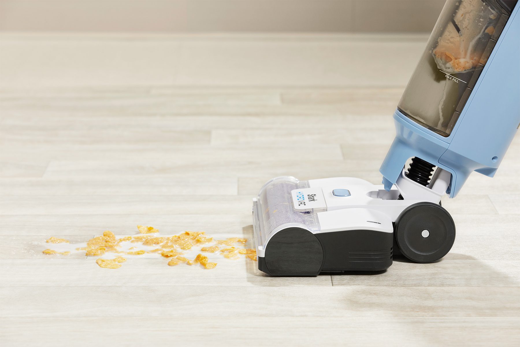 Vacuum cleaner absorbs cereal and milk spill on a light wood floor.
