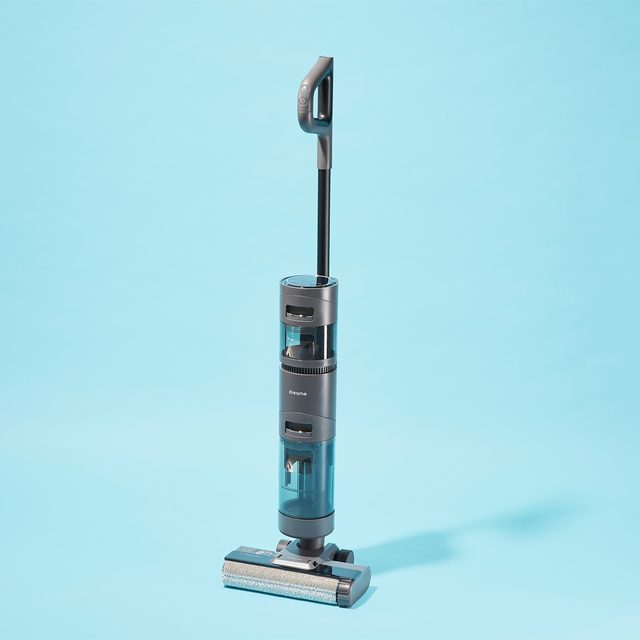 A vacuum cleaner stands upright on a clear blue background, showing a sleek, modern design with a long handle and transparent sections.