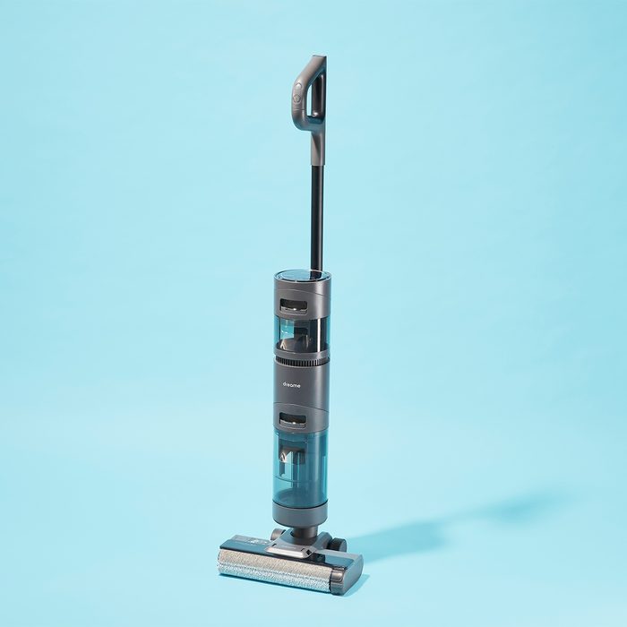A vacuum cleaner stands upright on a clear blue background, showing a sleek, modern design with a long handle and transparent sections.