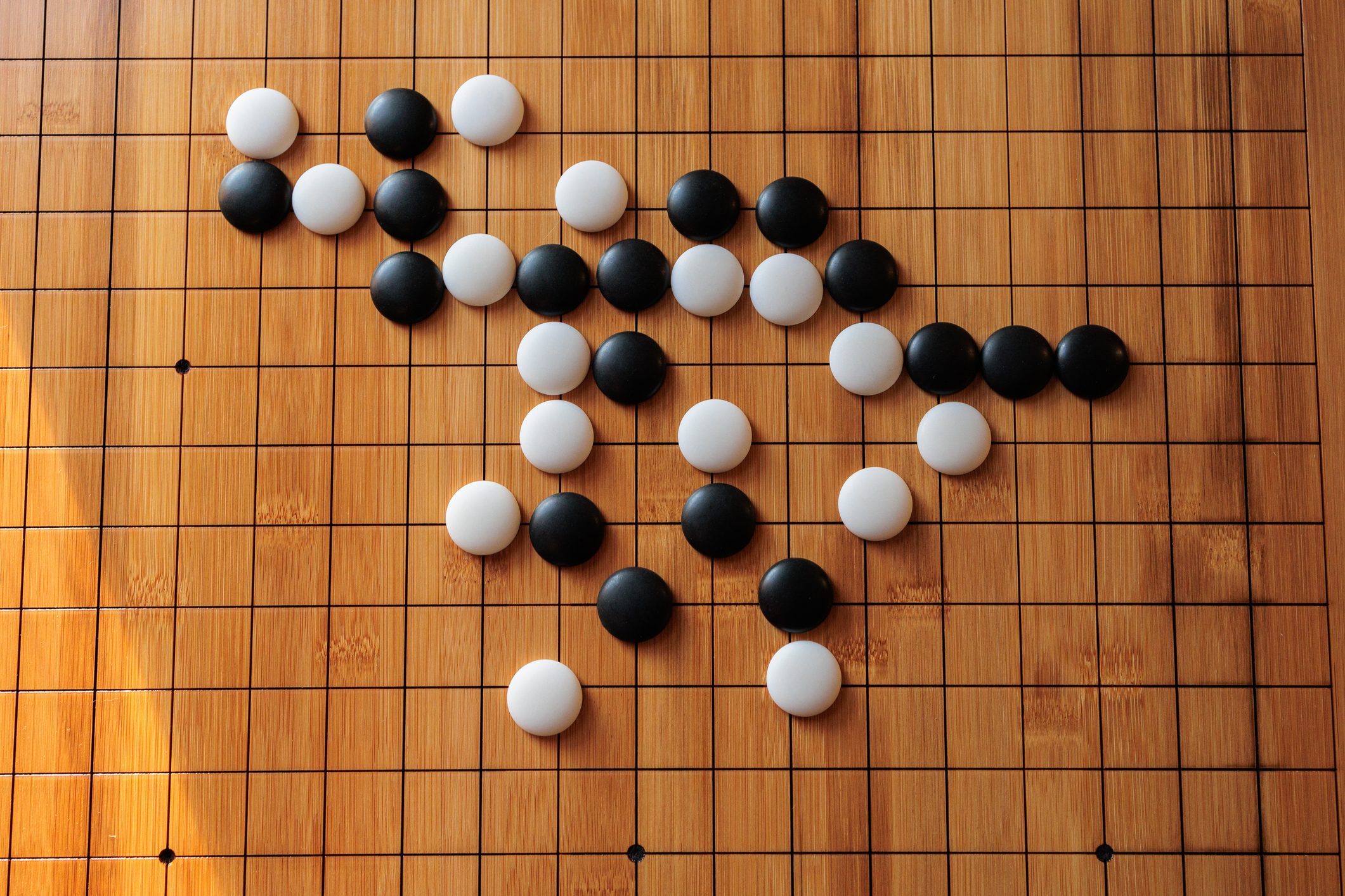 Black and white stones are placed on a wooden Go board, creating strategic patterns surrounded by grid lines.