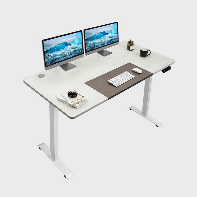 A modern desk holds dual monitors displaying ocean scenes, a keyboard, mouse, a small plant, a mug, and a book titled 
