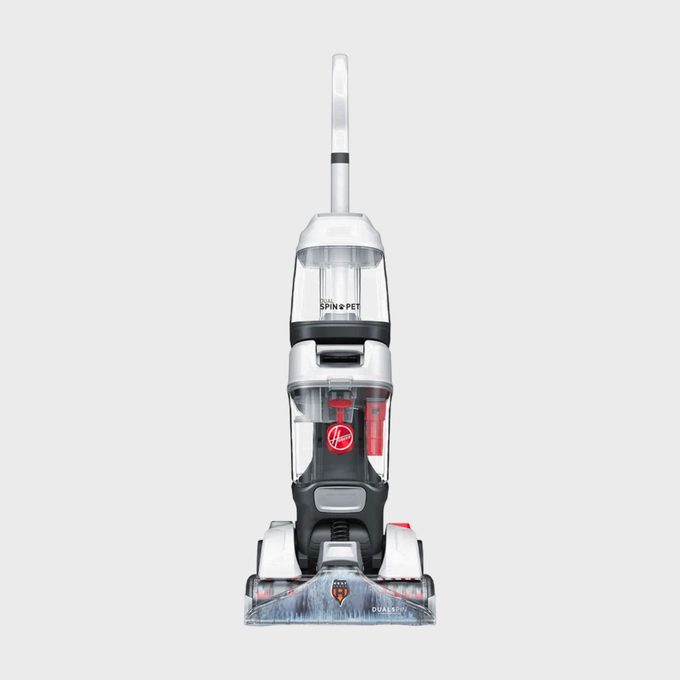 Upright vacuum cleaner stands idle; clear design reveals dust compartment; positioned against a plain, gray background with 