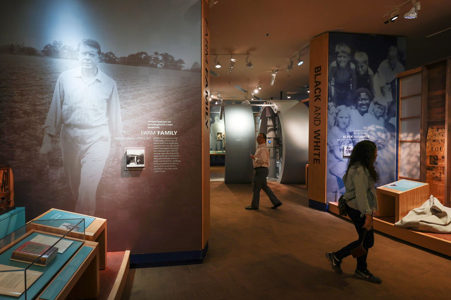 Museum exhibit featuring enlarged farm family portrait, visitors walking, surrounded by informative displays and text about Carter's farm and family history.