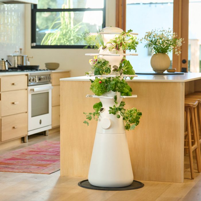 A vertical white planter with various green plants grows in a modern kitchen, beside a wooden island and stove, under natural light.