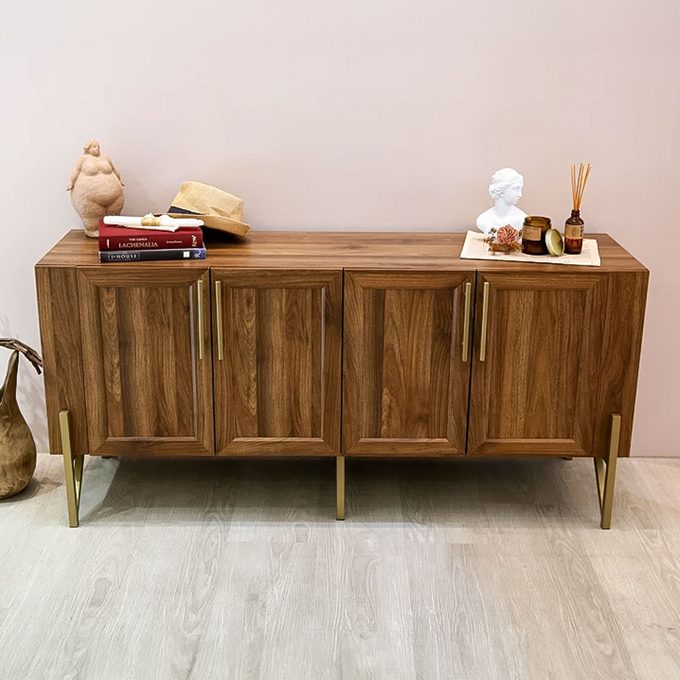 Wooden sideboard displays books, statue, and decor. Items arranged neatly on top in a minimalist room with a light wood floor.