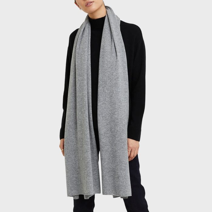 Gray scarf drapes over person's shoulders, wearing a black sweater, standing against a plain, light background.