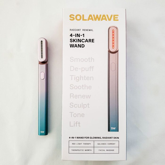A skincare wand rests next to its box; text highlights features like red light therapy, galvanic current, therapeutic warmth, and facial massage.