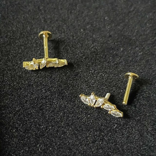 Gold earrings with small clear stones rest on a textured black surface.
