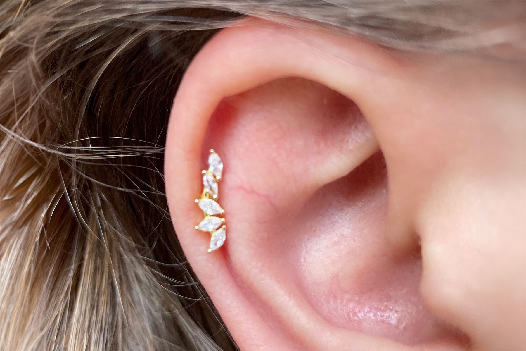 Earring with marquise-cut gems decorates an ear, surrounded by blonde hair strands.