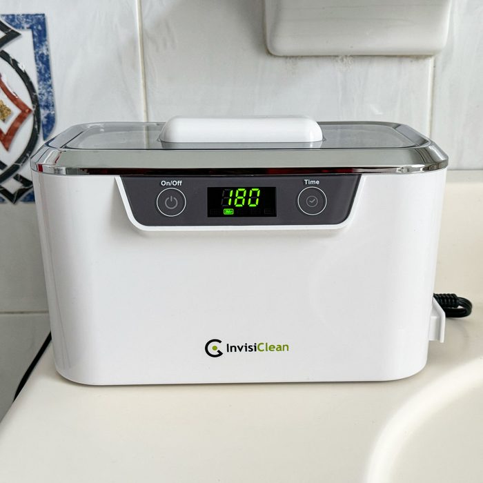 White ultrasonic cleaner displays 180 seconds on timer, placed on a bathroom counter.