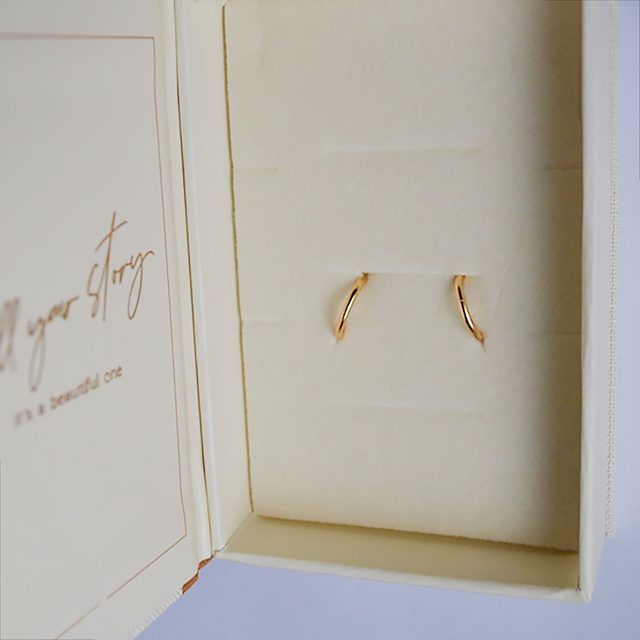 Earrings rest on a card inside an open box, with cursive text reading 