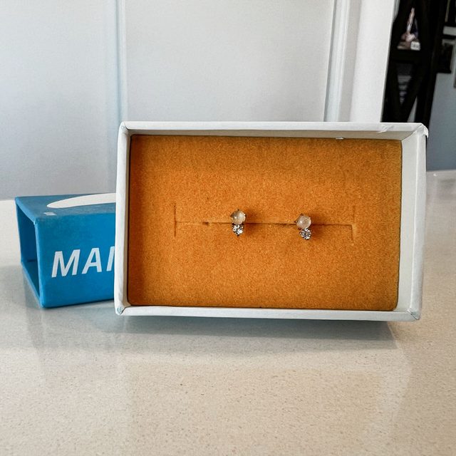 Earrings resting inside an open jewelry box on a countertop, with a blue box labeled 