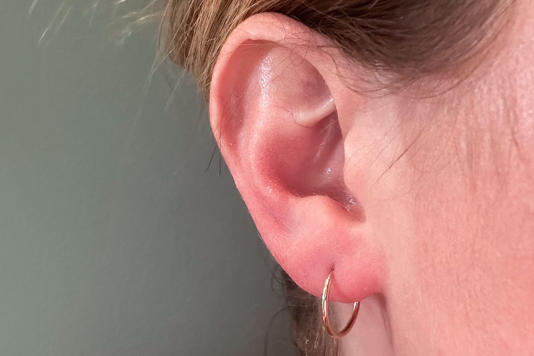 An ear with a small, gold hoop earring is visible against a neutral background.