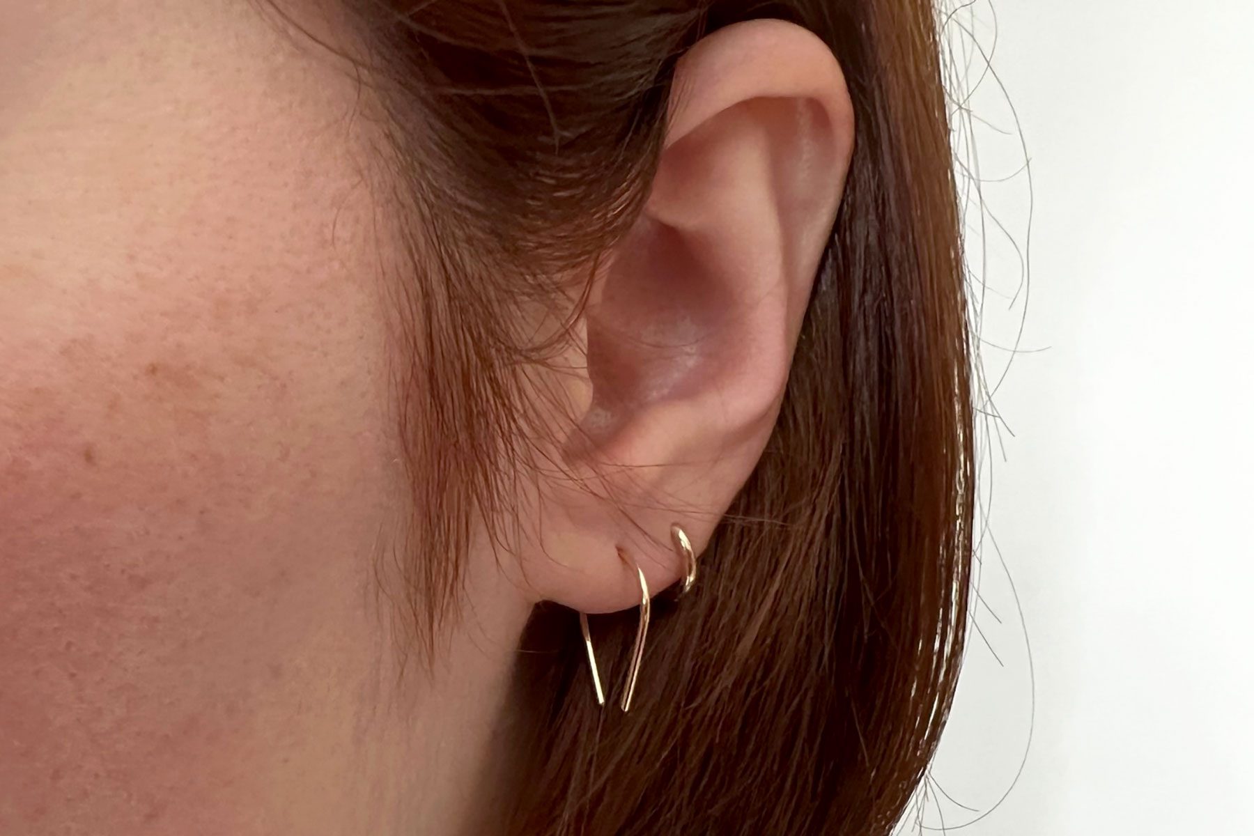 Earring adorns ear, hanging delicately alongside brown hair in a neutral setting.