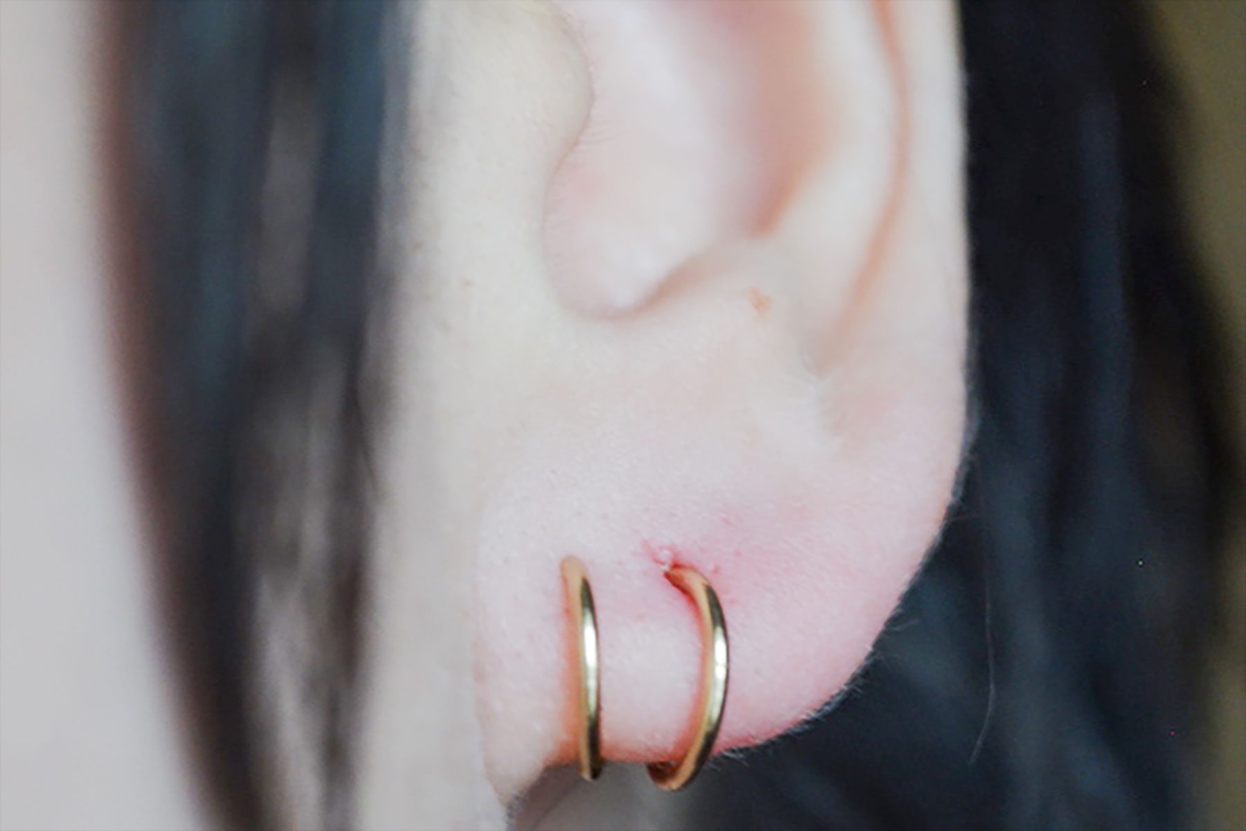 Two gold earrings adorn an ear, surrounded by dark hair.