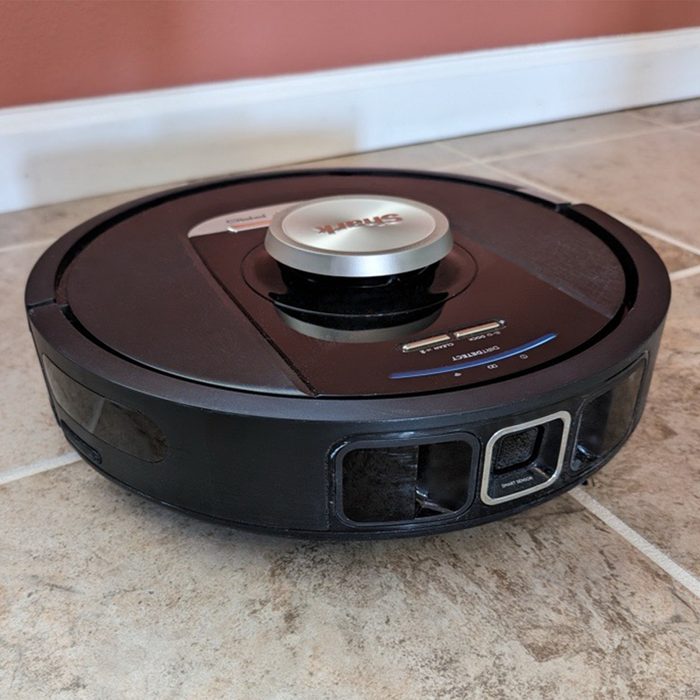 Robot vacuum sits idly on tiled floor near a peach-colored wall, with 