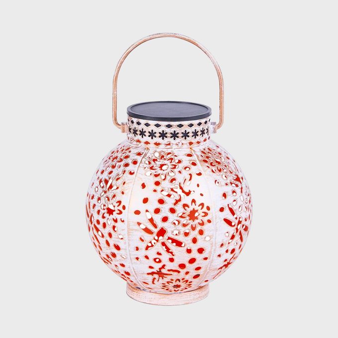 A round, intricately patterned lantern rests with a handle, showcasing floral cutouts. It is set against a plain white background.