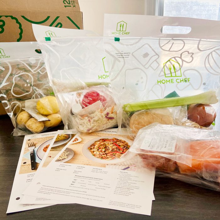 Meal kit ingredients arranged on a table with recipes in a kitchen setting; labeled 