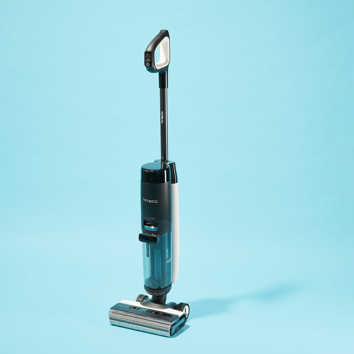 Vacuum cleaner stands upright on a light blue background, displaying brand logo on its body.