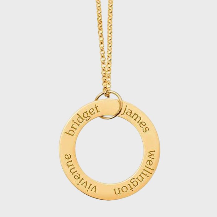 A gold ring pendant hangs on a chain, engraved with names: bridget, james, wellington, viviane, set against a plain white background.
