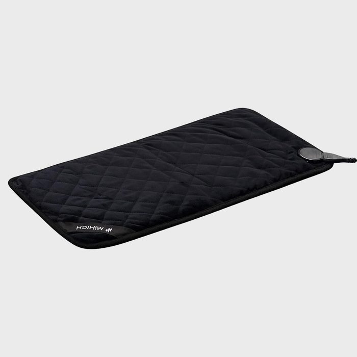 A quilted black heating pad lies flat, featuring a power cord and control dial in a plain, neutral background.